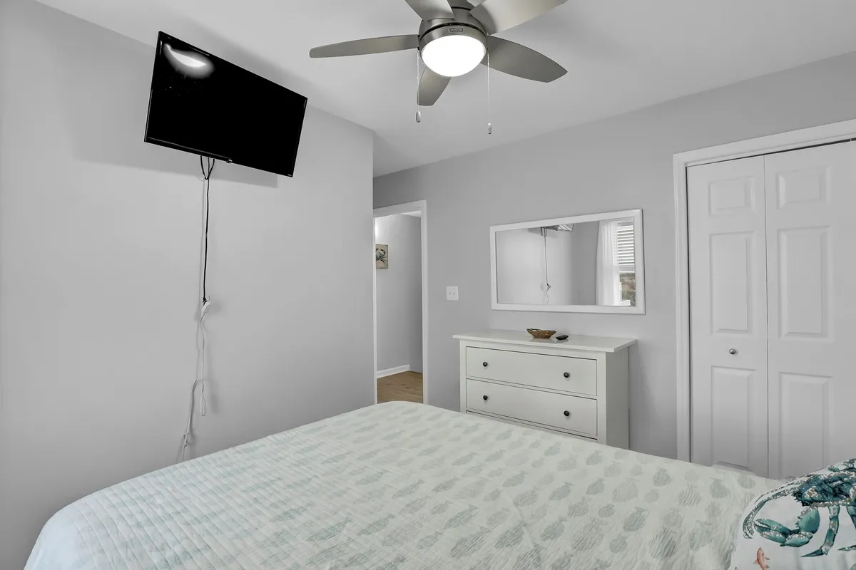 A tranquil bedroom featuring a king-size bed with a textured quilt, a ceiling fan overhead, a wall-mounted television, and a dresser with a mirror. The soft lighting and inviting bedding create a peaceful and private retreat within the home.