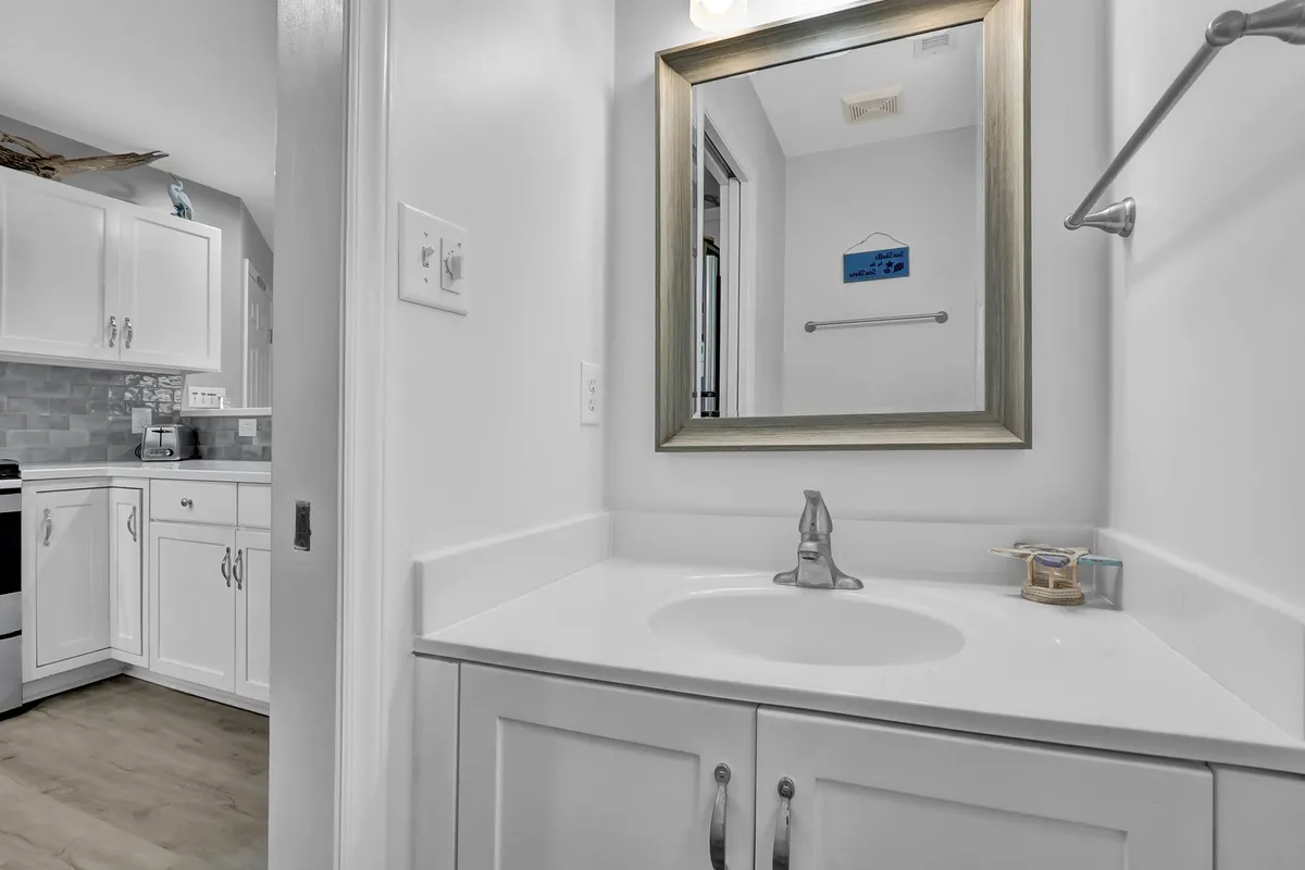 A refreshing bathroom featuring a well-lit mirror, modern sink, and white cabinetry. The clean, crisp design makes it an inviting space for self-care and quick freshen-ups.