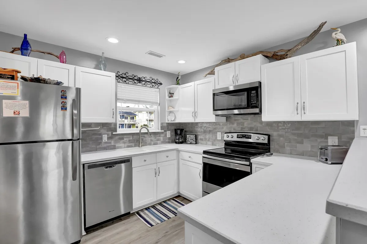 A bright, welcoming kitchen featuring stainless steel appliances, crisp white cabinetry, and a central island. Natural light fills the space, and the open layout suggests easy flow between kitchen, dining, and living areas.
