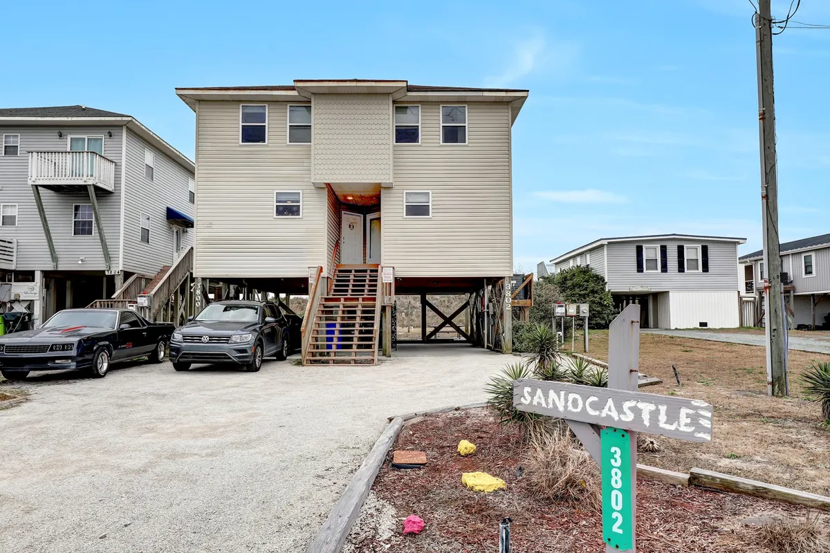 This image features the exterior of the oceanfront duplex labeled 'SANCASTLE,' with ample parking and a welcoming front porch. The setting hints at the relaxed, communal atmosphere ideal for group gatherings. The home's position suggests easy access to the beach and communal outdoor activities.