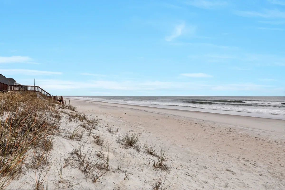 A peaceful beach scene with gently rolling sand dunes and ocean waves under a wide sky. The open shoreline offers ample room for walking, playing, and exploring with pets.